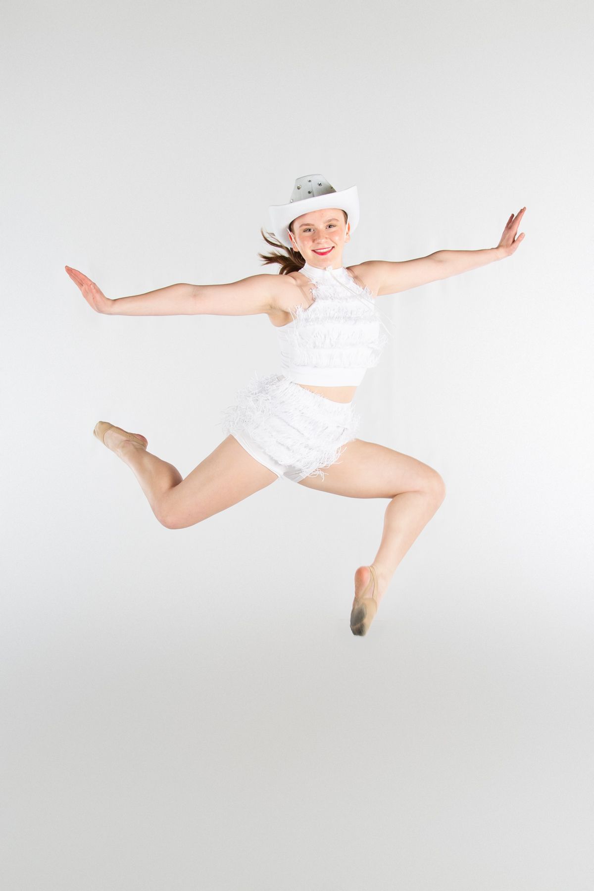 A dancer in white performs a graceful leap against a plain studio backdrop.
