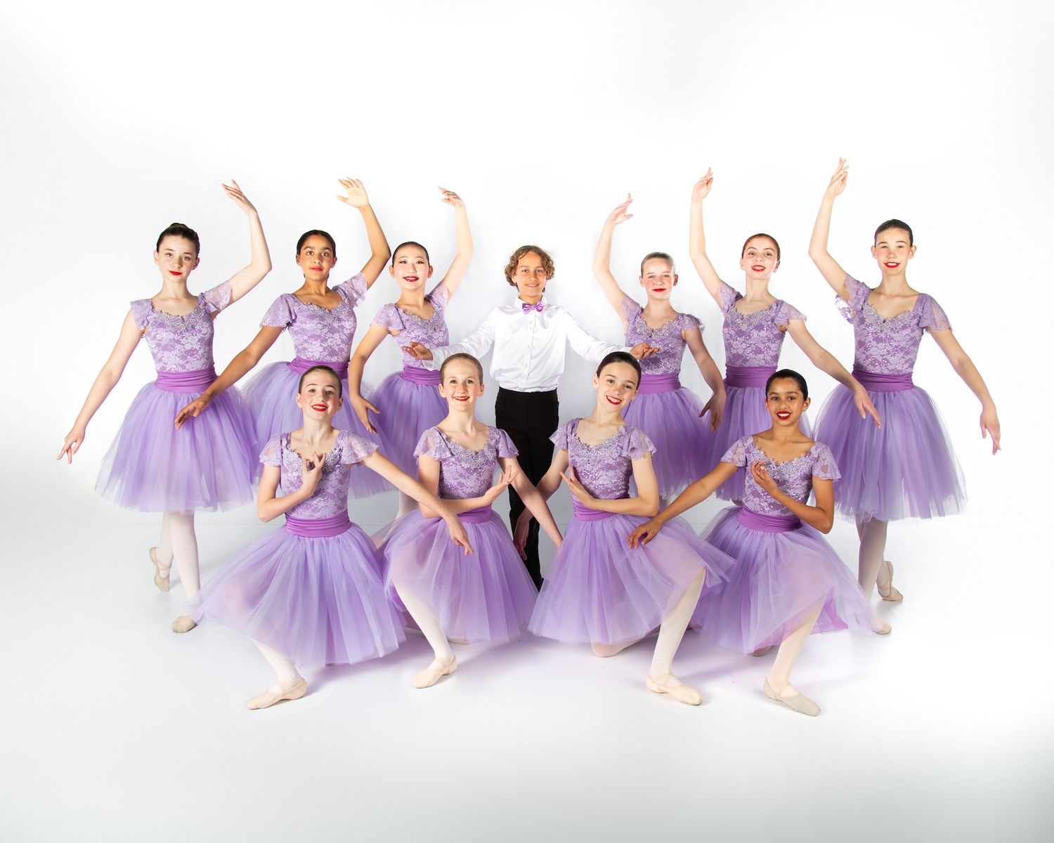 Ballet ensemble in lavender tutus strikes synchronized pose during group performance.