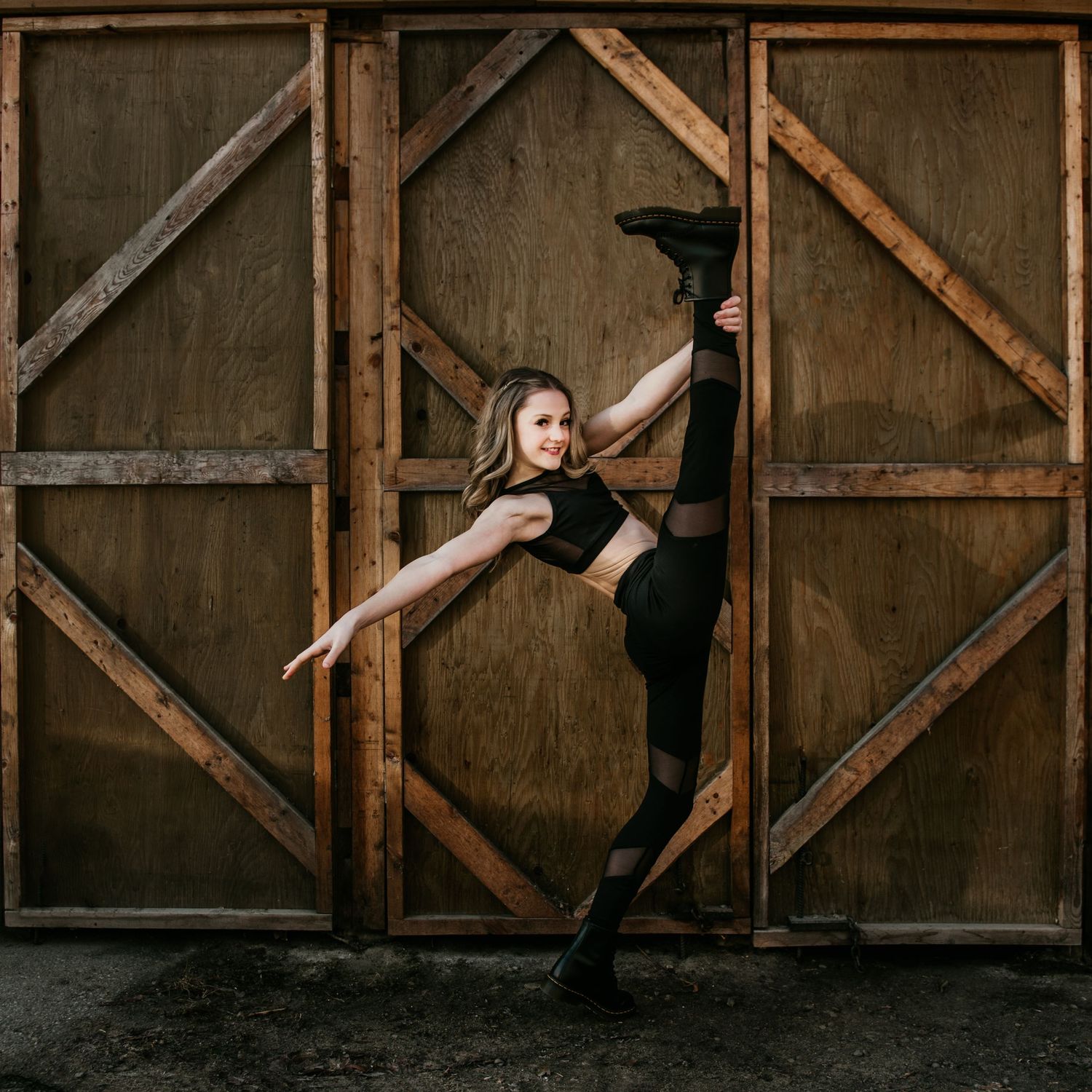 A dancer in black attire performs a dramatic split pose against a wooden geometric backdrop.