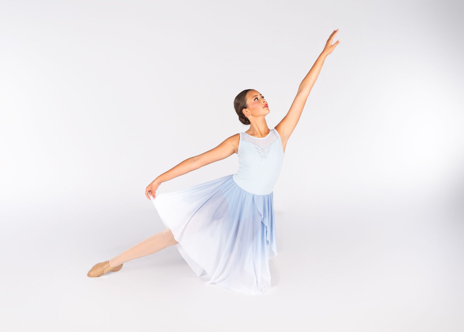 A ballet dancer in a flowing white dress performs an elegant arabesque pose against a light gray background.