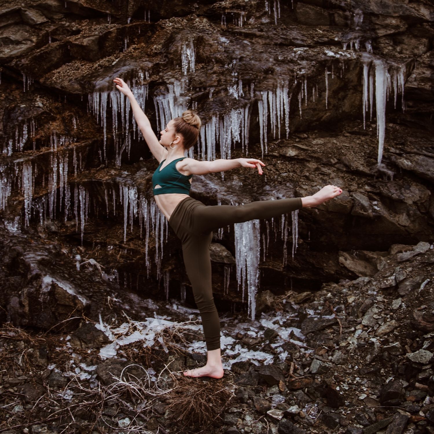 A dancer strikes a graceful pose in front of an icy rock face with dramatic icicles hanging from above.