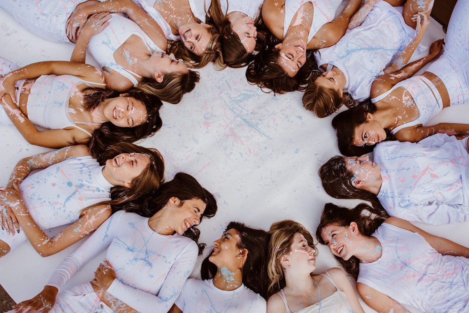 Group of people lying on the ground in white dresses arranged in a circle formation creating a unique overhead view.