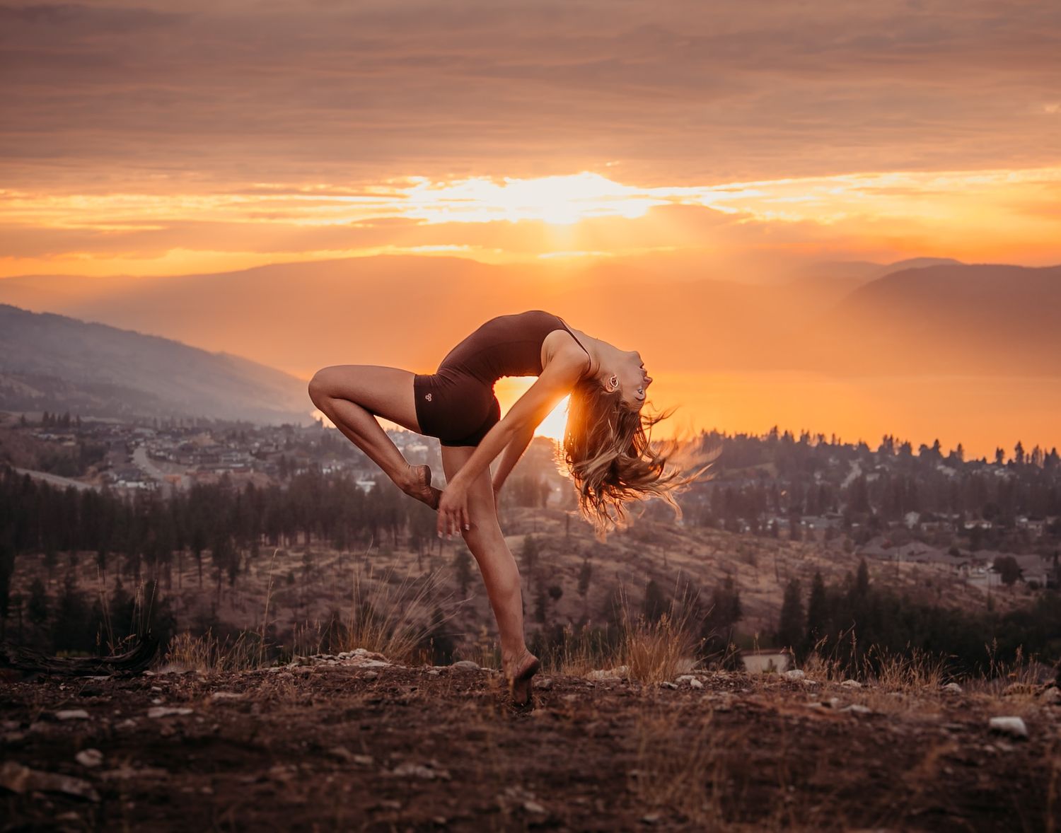 Artistic dance pose silhouetted against vibrant orange mountain sunset landscape.