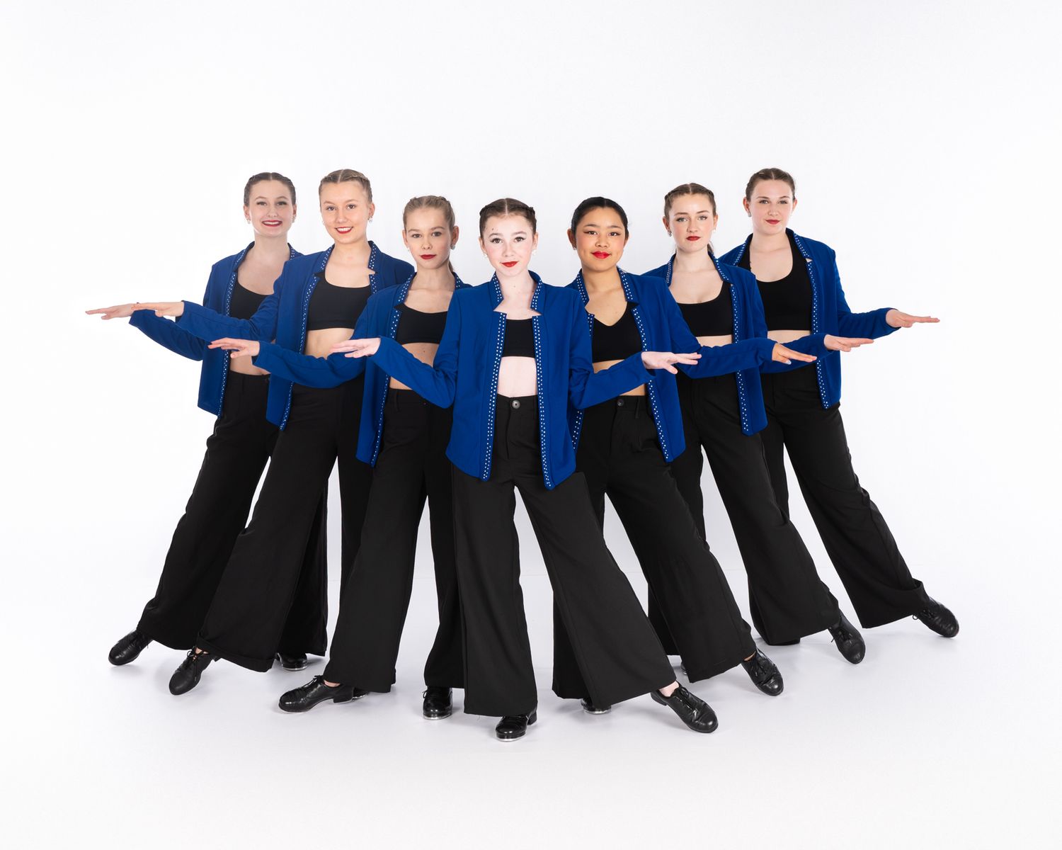Dance performers in matching navy blue tops and black pants strike a synchronized pose against white background.