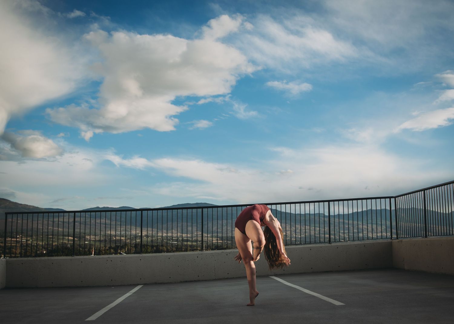 A graceful dance pose captured against a scenic mountain backdrop in a rooftop parking area.