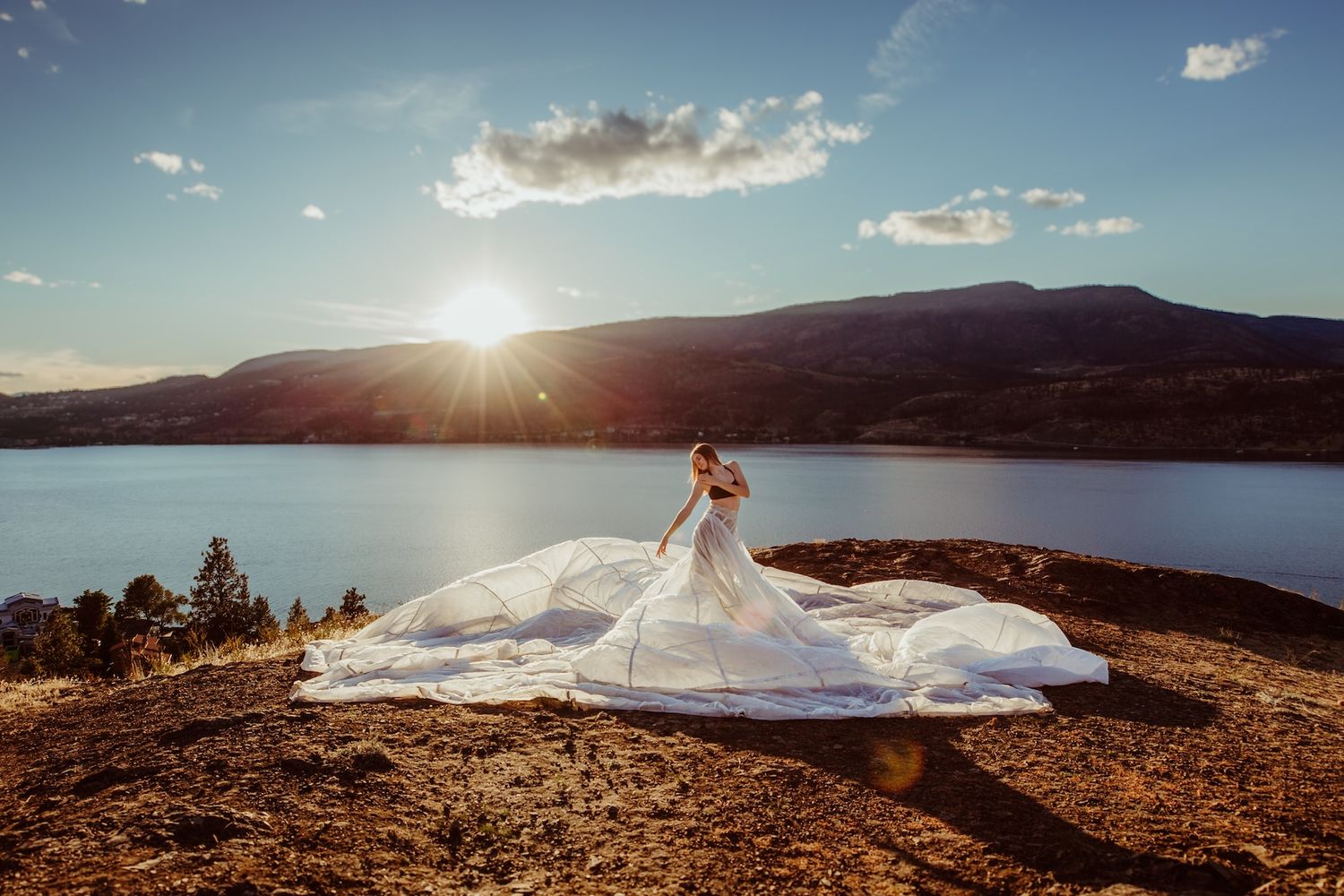 A scenic mountain lake at sunset with a long flowing white dress displayed on rocky terrain overlooking the water.