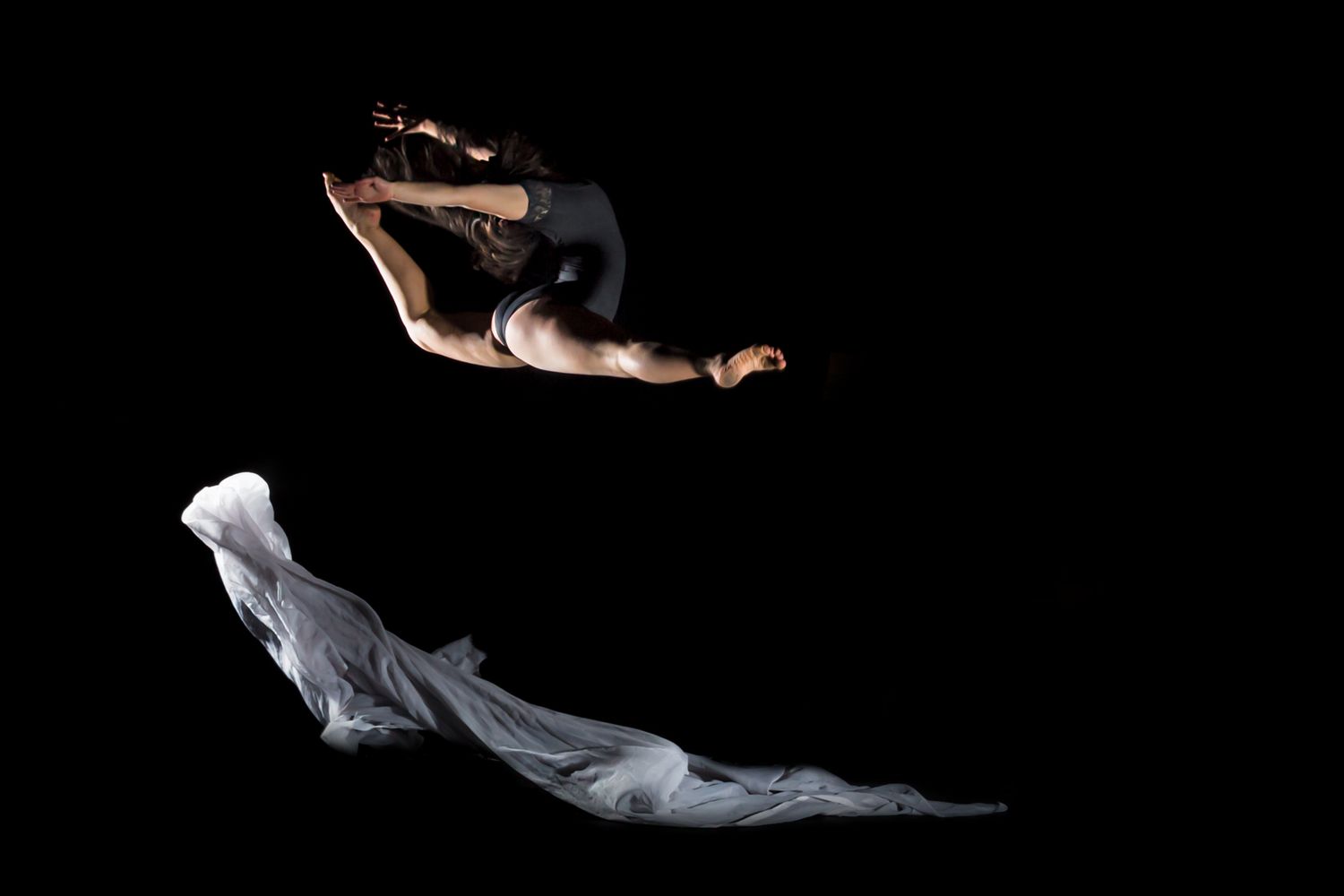 Two dancers perform a dramatic leap and floating movement against a black background in artistic dance photography.