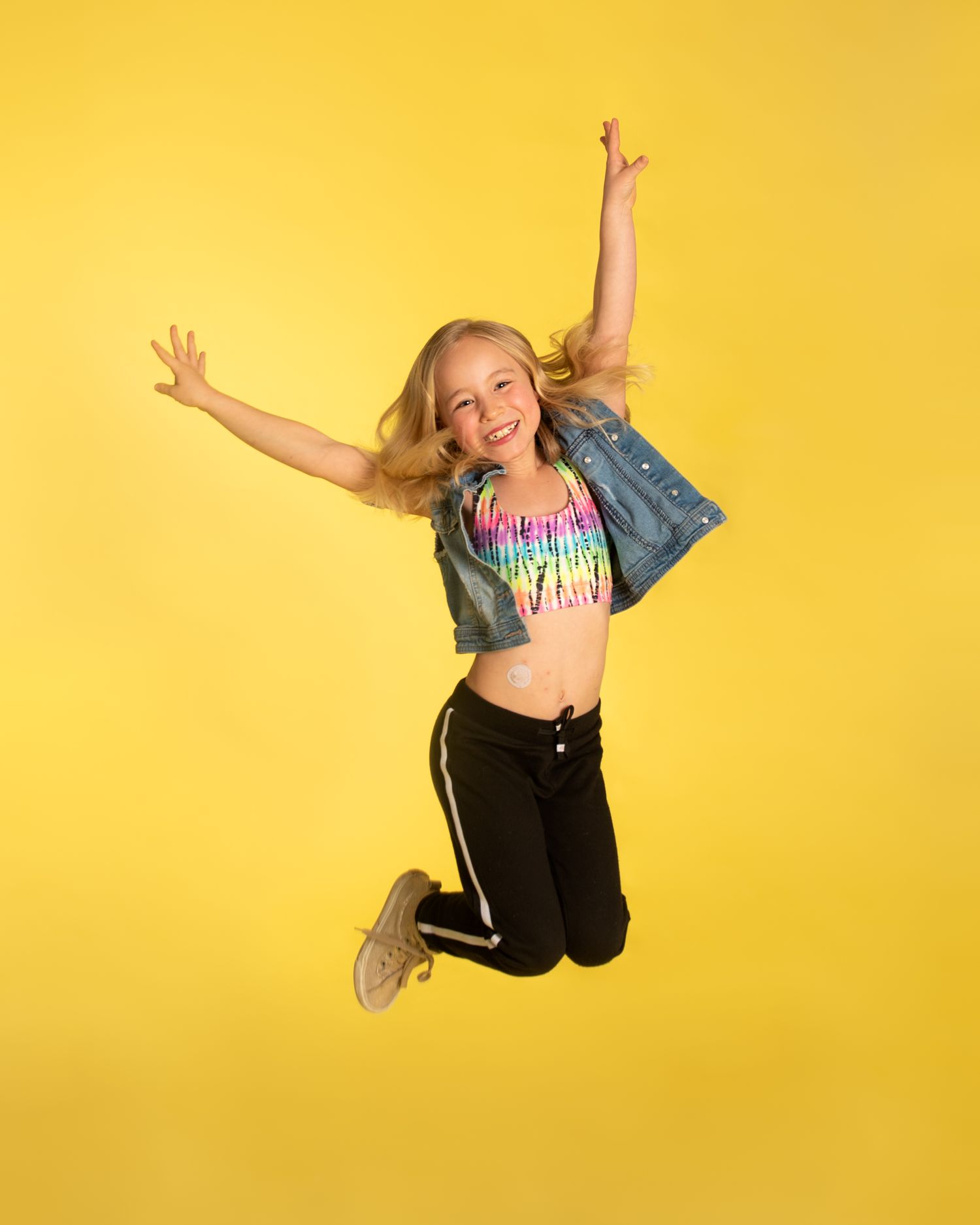 An energetic dancer in denim and crop top jumps against a bright yellow background.