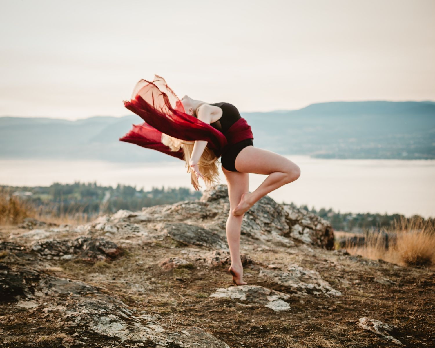 Dynamic dance movement with red fabric against mountain and lake backdrop.