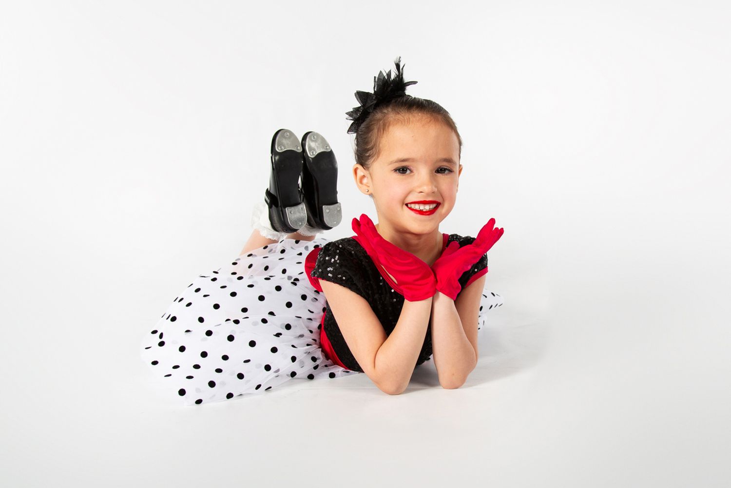 A dancer in polka dot tulle rests on the floor in a playful pose against a white background.