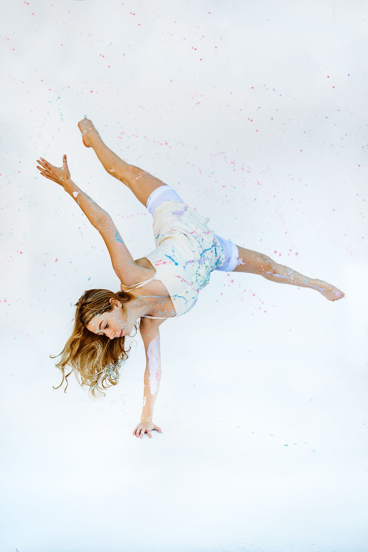 Dancer performs an inverted handstand pose with dramatic hair motion against light background.
