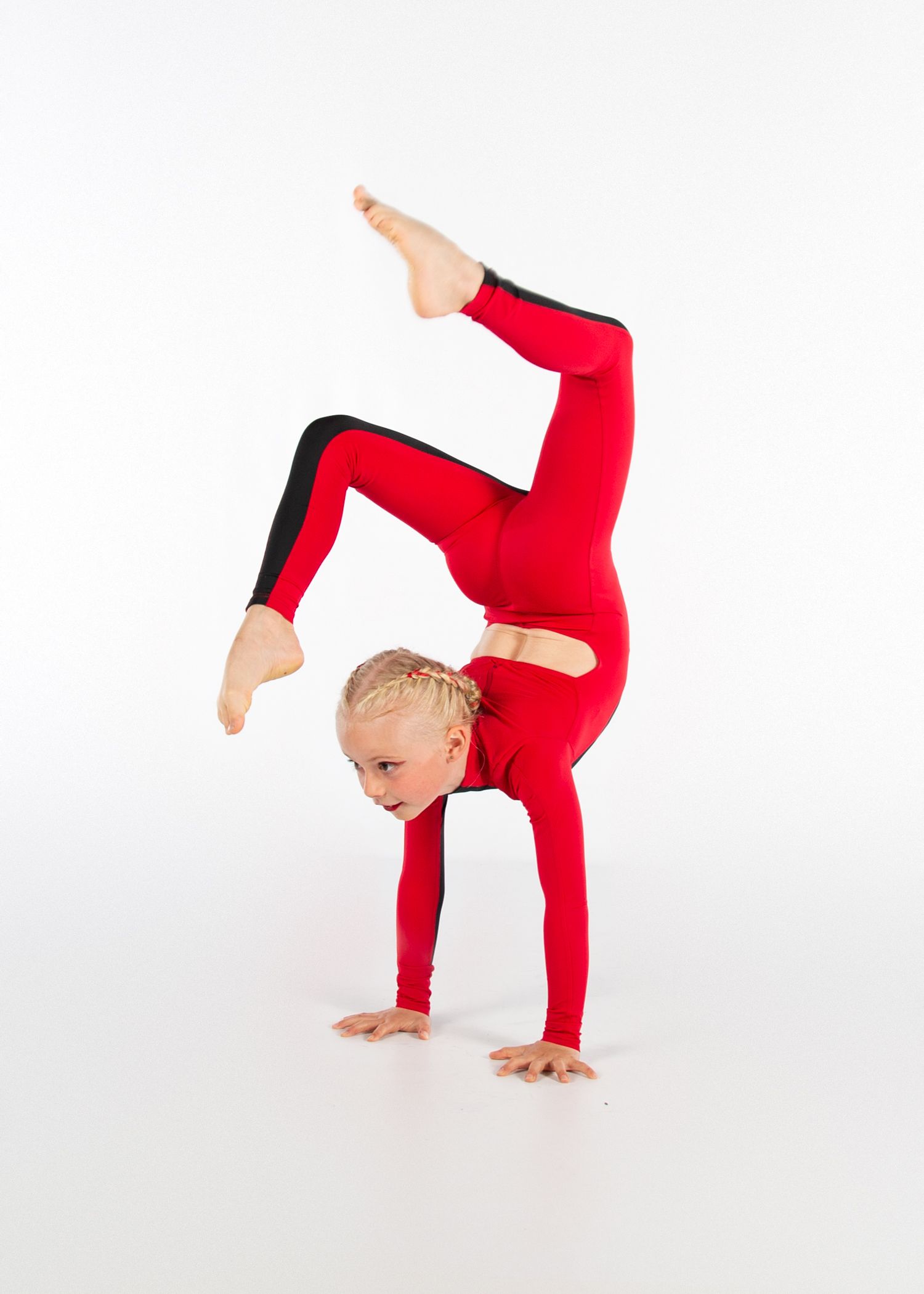 Young gymnast in red unitard performs a handstand with split legs against white background.