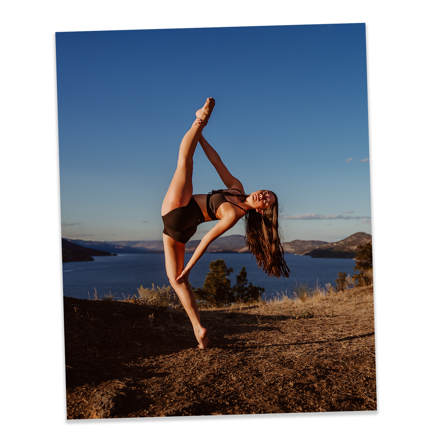 Dancer performs graceful splits pose against scenic mountain lake backdrop during golden hour sunset.