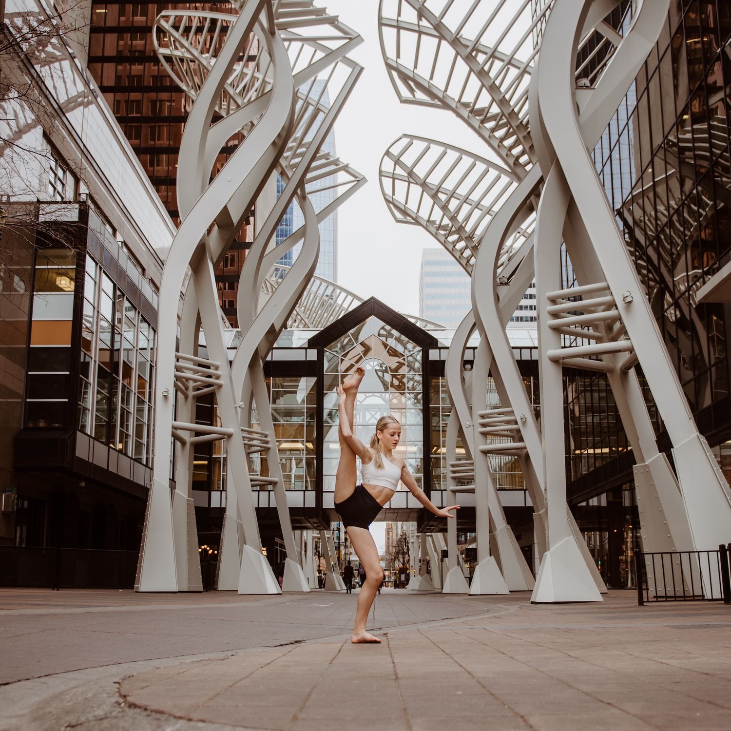 Dancer strikes an elegant pose between modern white tree-like architectural structures in an urban setting.