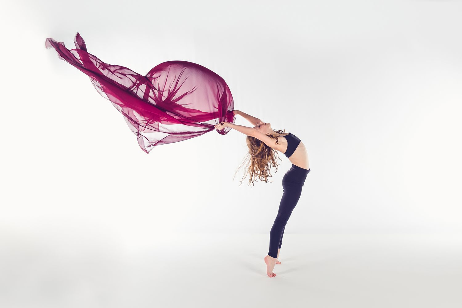 Contemporary dancer in dynamic backbend pose with flowing magenta fabric against white background.