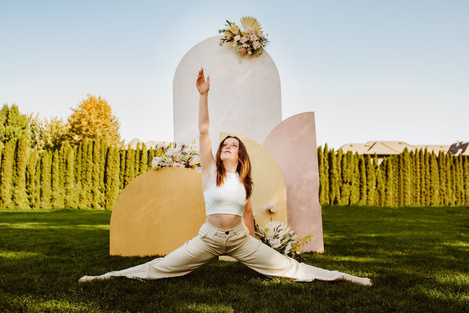 Graceful dancer performs splits in front of elegant curved backdrop with floral decor in outdoor garden setting.