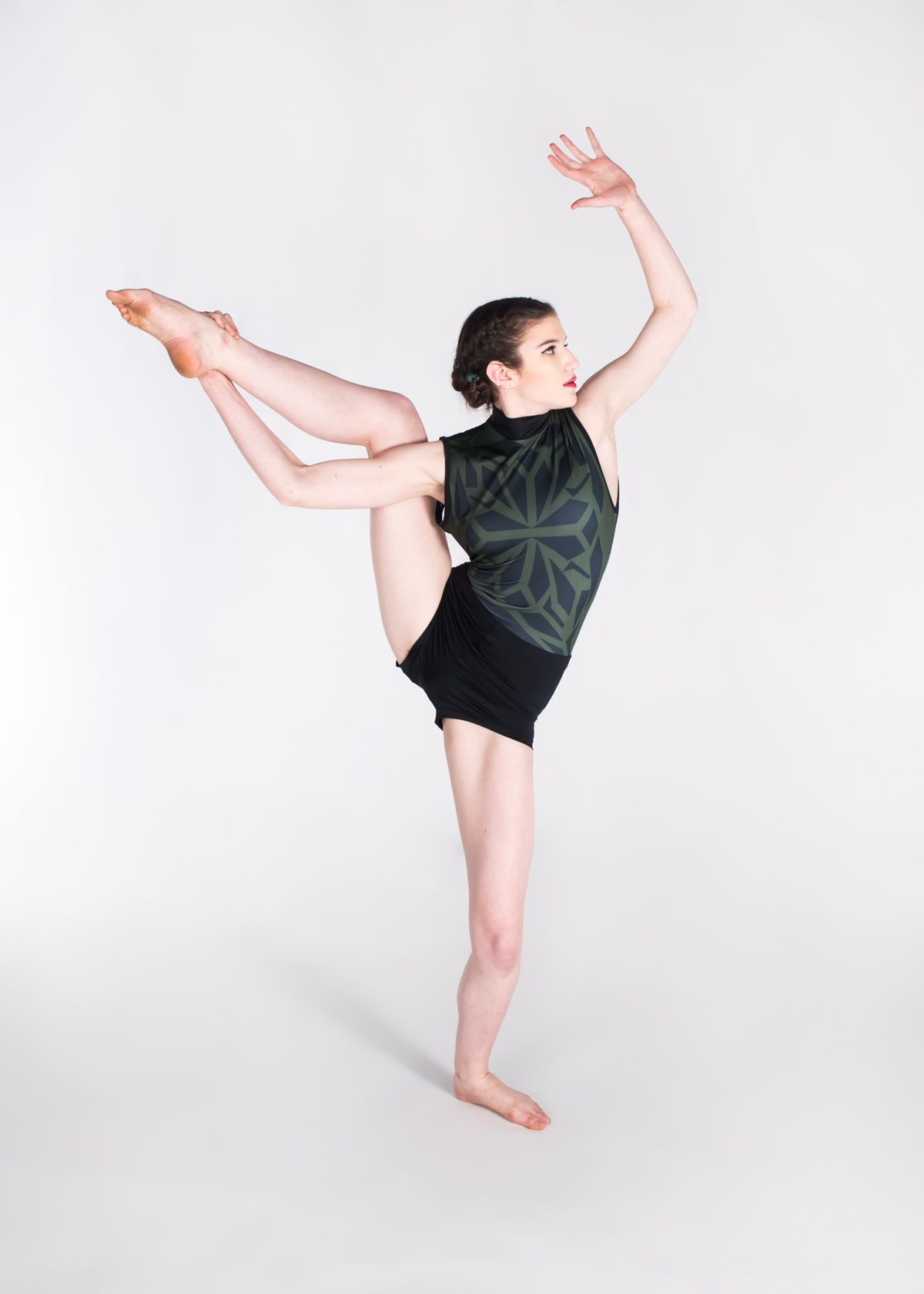 A dancer in black attire performs a striking split pose with raised arms against a white studio backdrop.