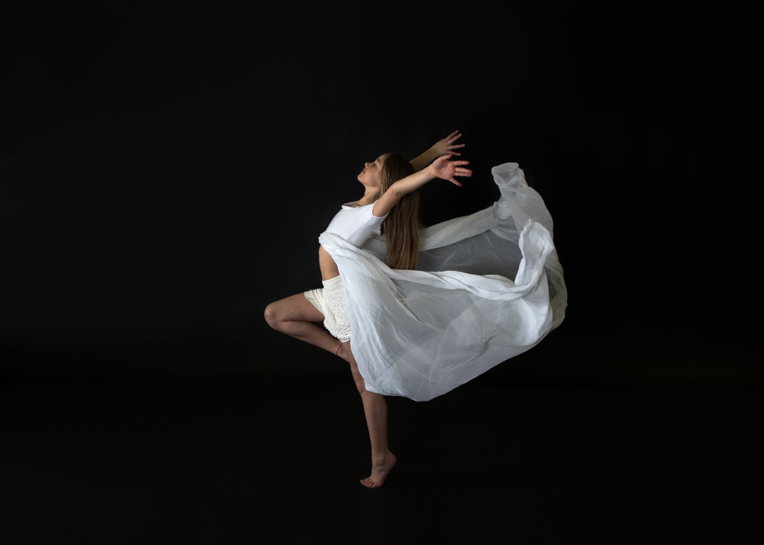 A contemporary dancer in flowing white dress spins expressively against a black background.