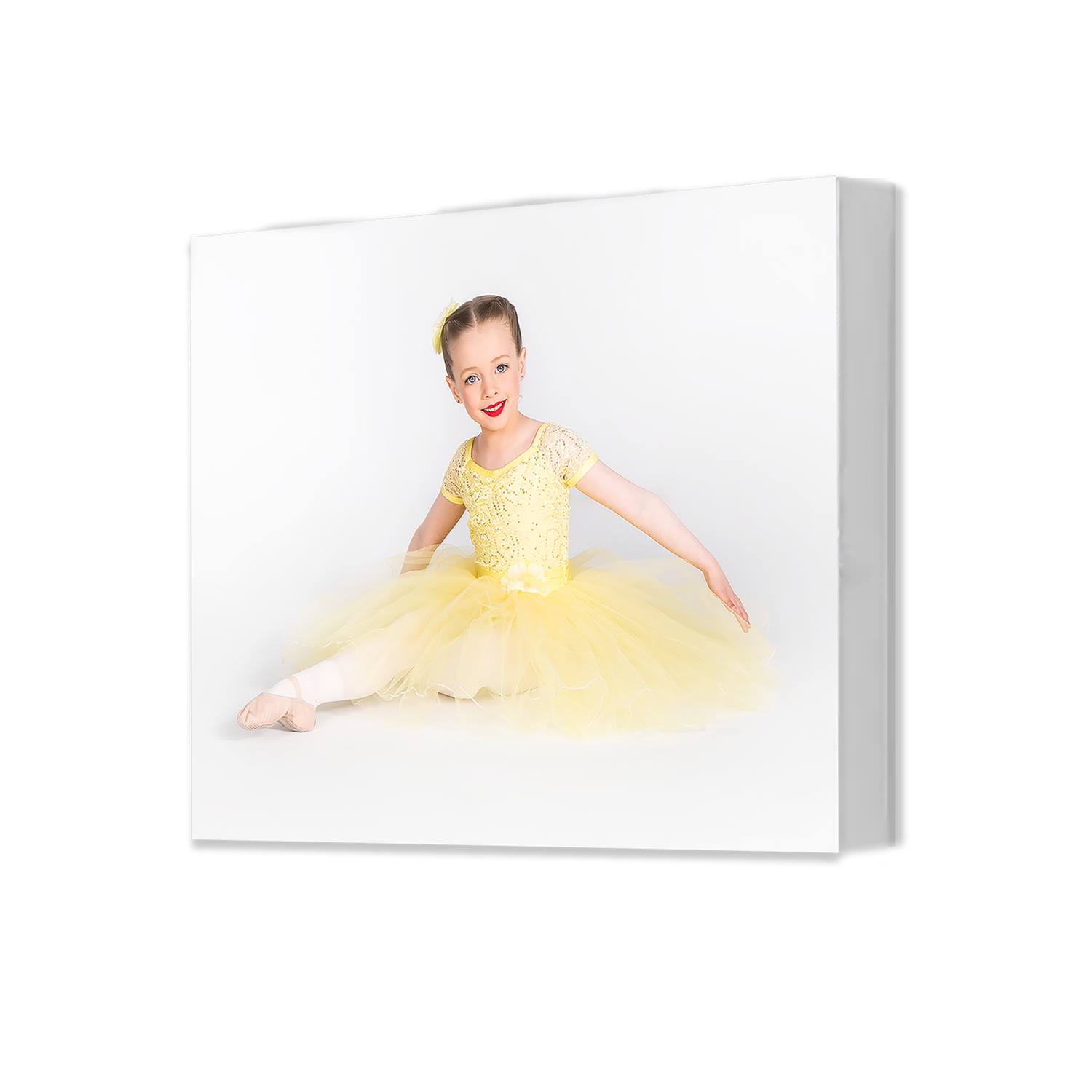 Young dancer in yellow ballet dress and pointe shoes gracefully poses on white background.