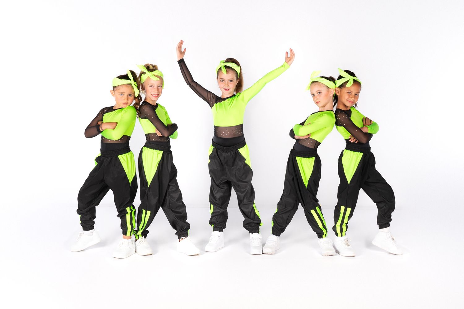 Dance group in black and neon green outfits performs energetic hip hop choreography in studio setting.