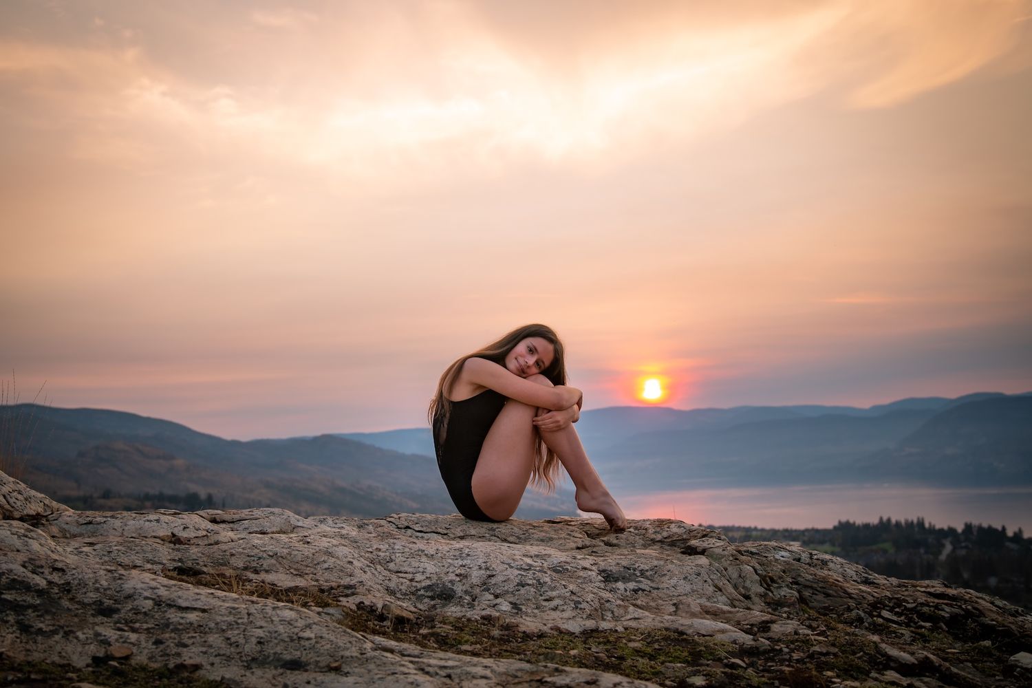 A silhouetted figure sits in contemplation on a rocky outcrop during a vibrant mountain sunset.