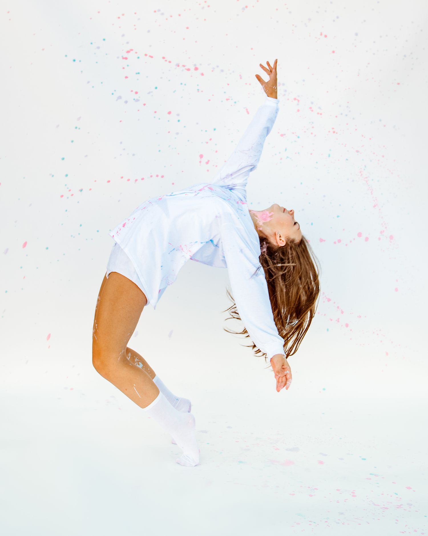 Dancer in flowing white outfit performs a dramatic backbend against a light background with pink confetti.