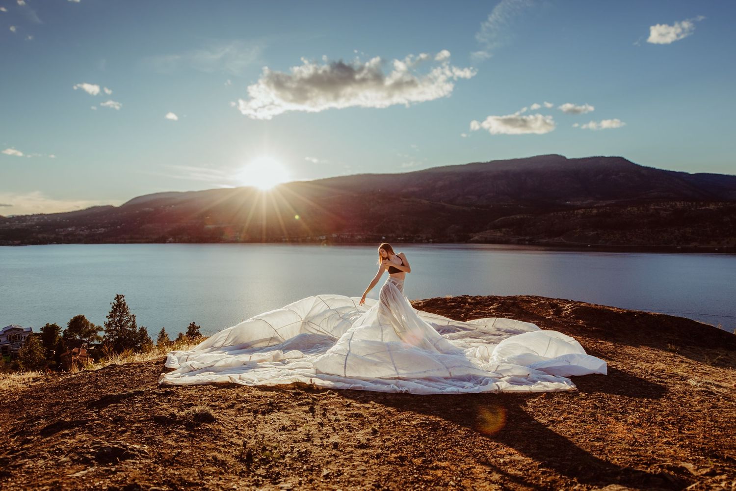 A stunning sunset at Lake Okanagan with a flowing white gown flowing in the breeze on a rocky overlook.