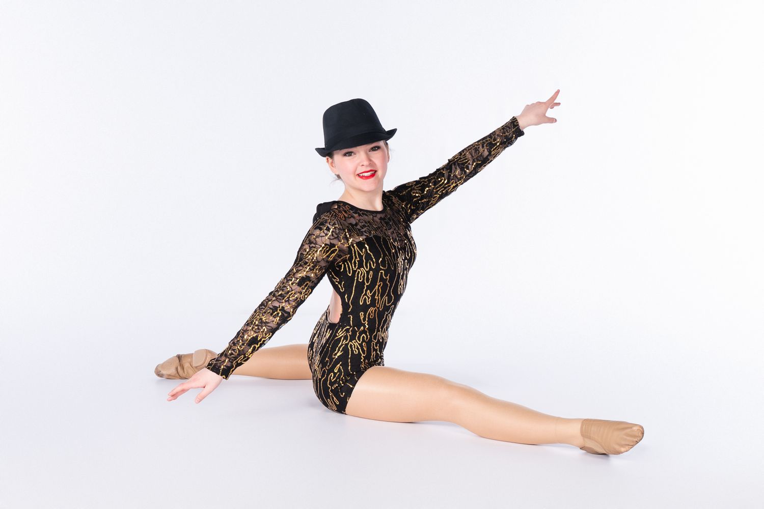 Dancer in black lace leotard and bowler hat performing jazz split leap.