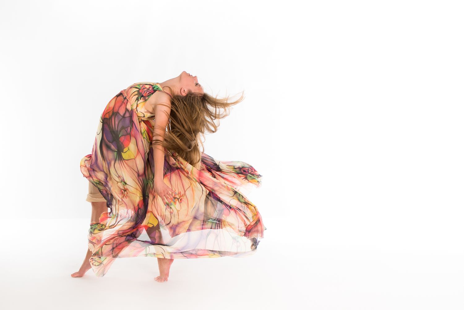 A dancer in flowing floral dress spins gracefully against a white background, creating movement with billowing fabric.