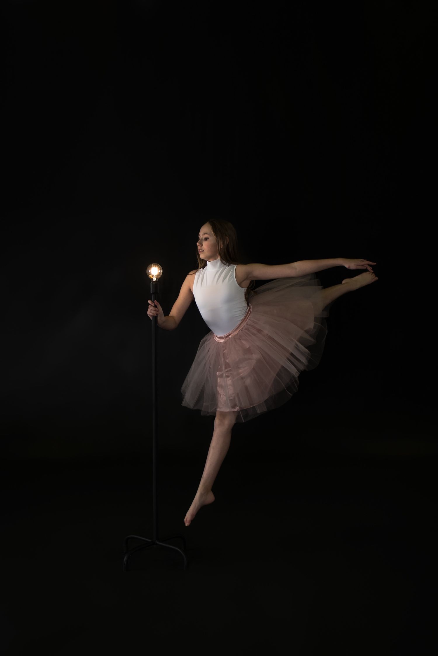 A ballet dancer in a pink tutu strikes an elegant pose while holding a glowing light stick against a dark background.