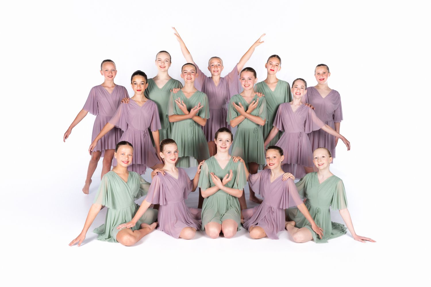 Dance performers in pastel purple and mint green costumes pose together in an artistic formation on white background.