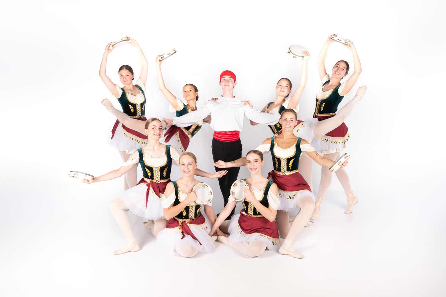 Ballet dancers in burgundy and white costumes pose gracefully together in a studio formation against white backdrop.