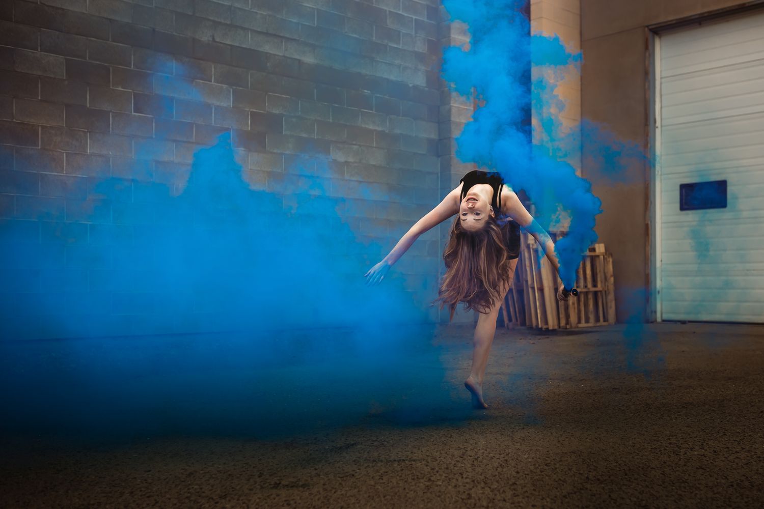 A dancer in a dress performs among dramatic blue smoke effects in a warehouse setting.