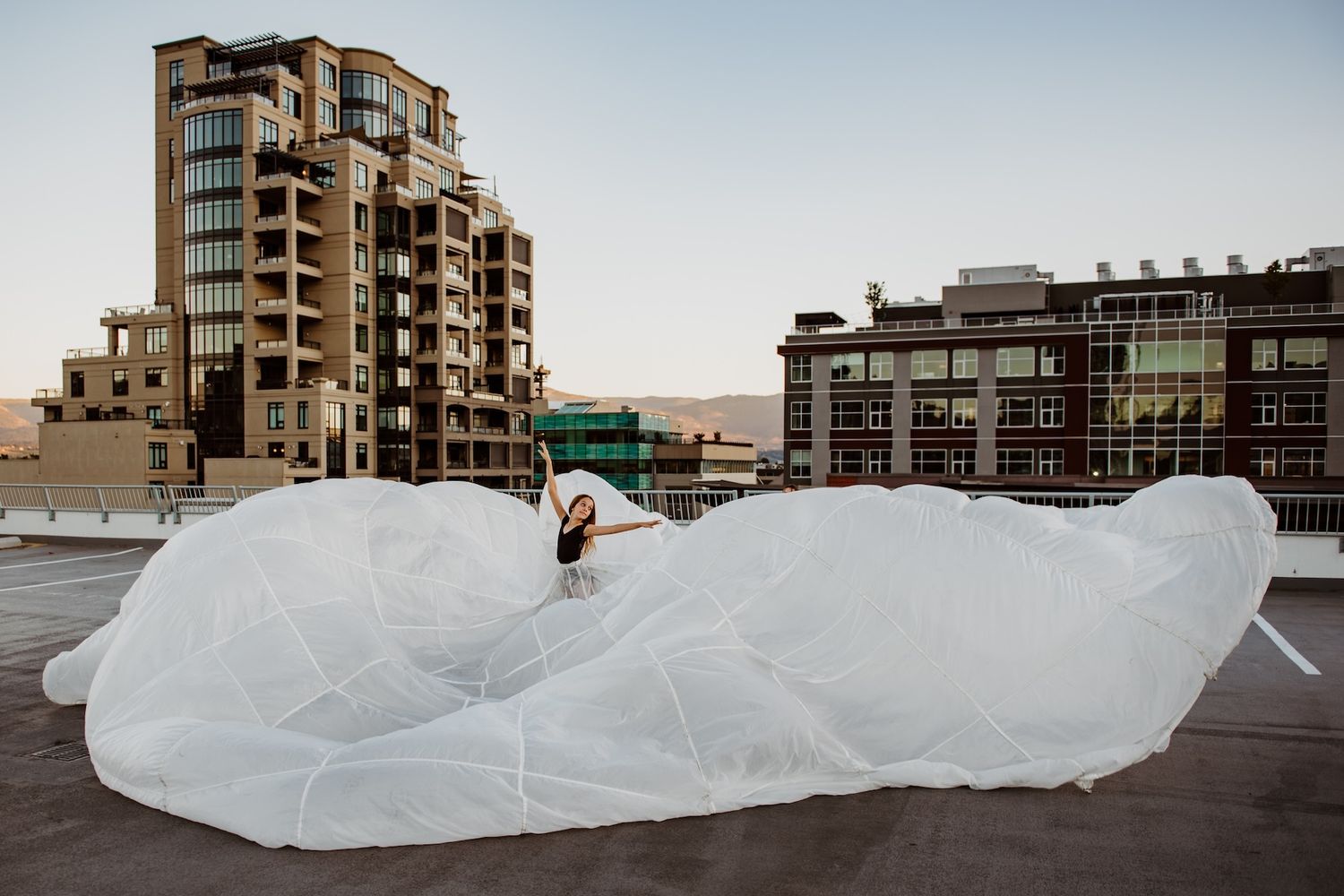 A person atop a large white billowing fabric installation on an urban rooftop with apartment buildings in the background.