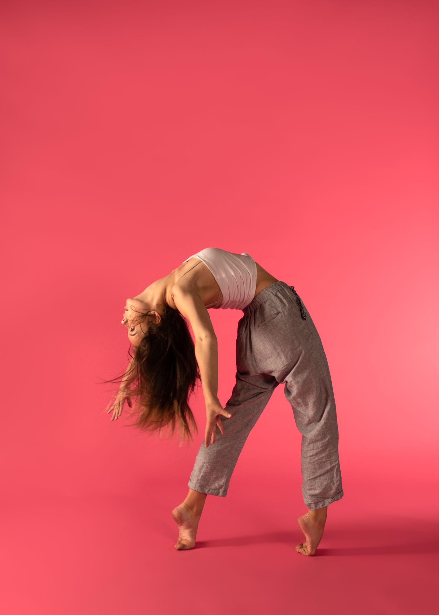 Dancer performing expressive contemporary dance movement in grey attire against vibrant pink backdrop.