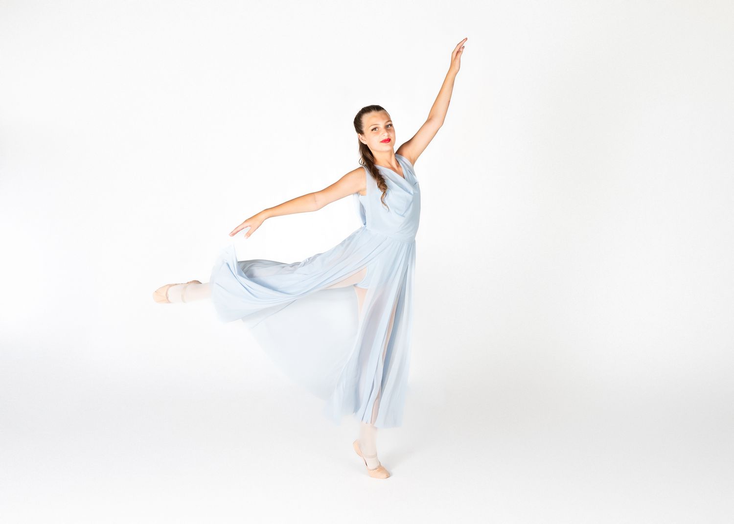 Dancer in flowing light blue dress strikes graceful pose on white background.