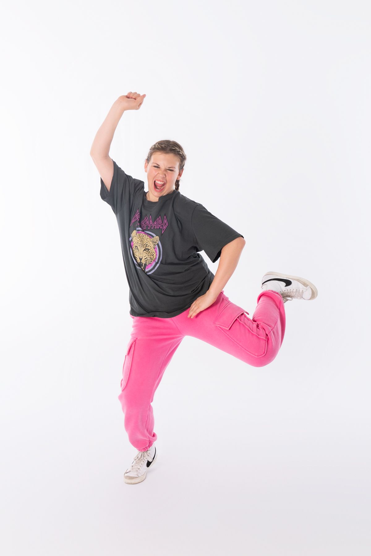 Energetic dancer in pink pants and black t-shirt leaps against white background.