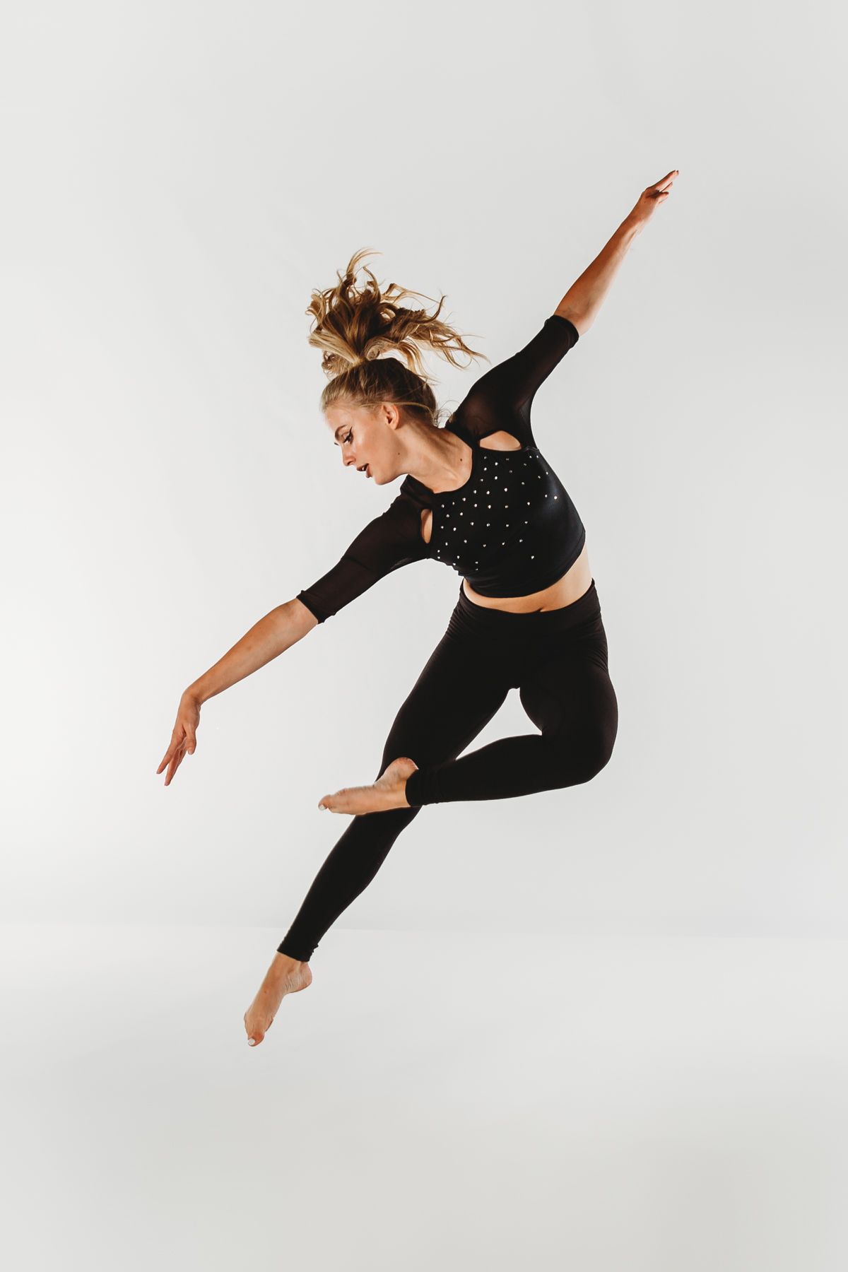 A dancer in black athletic wear leaps gracefully through the air against a white background.