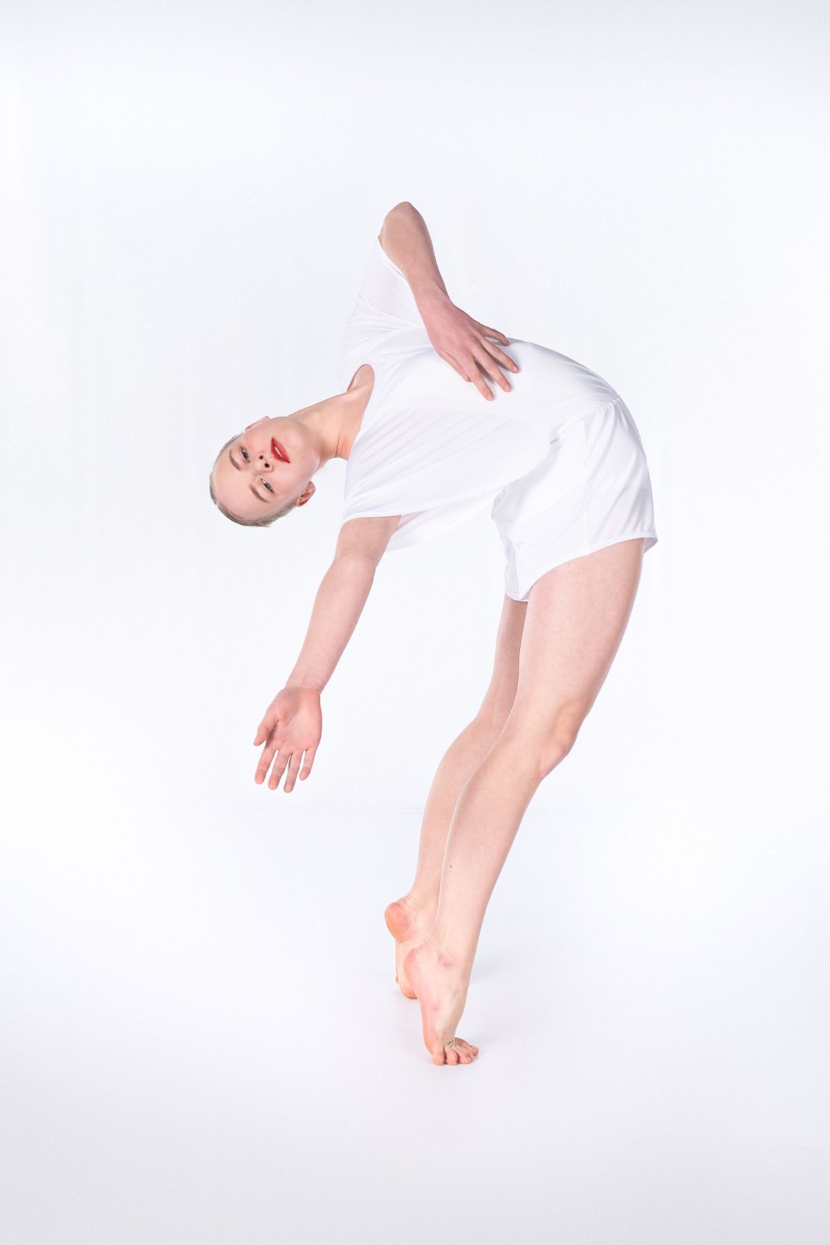 A dancer in white performs a graceful backbend pose on a light background.