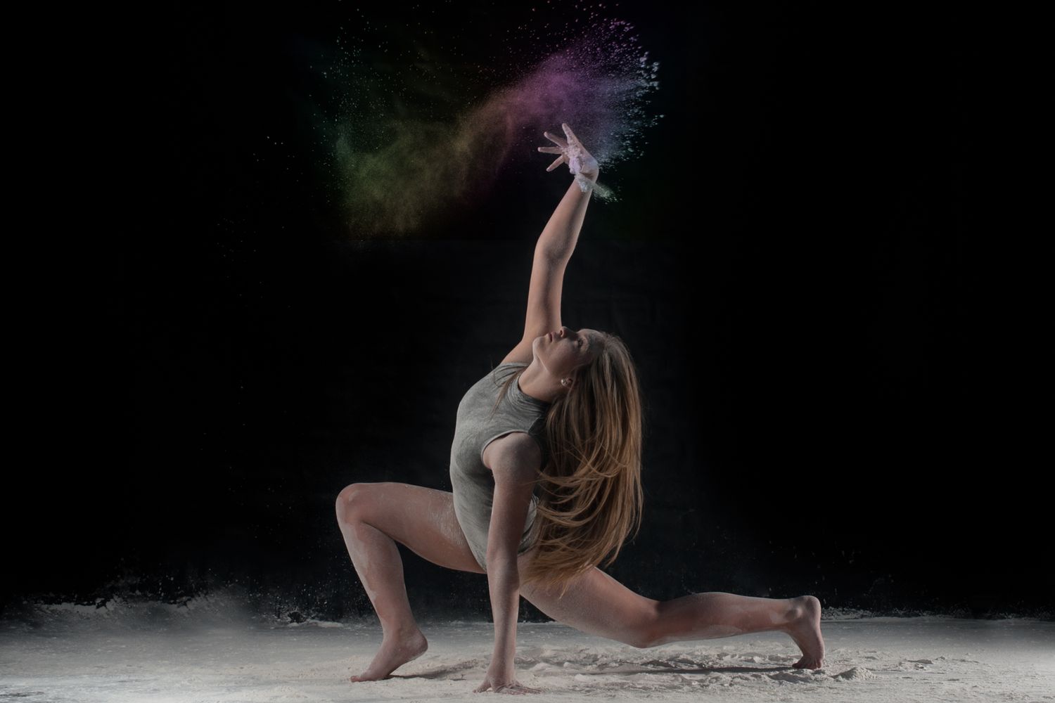 Dancer in dramatic pose creating colorful powder cloud effect against dark background as flour billows around movement.