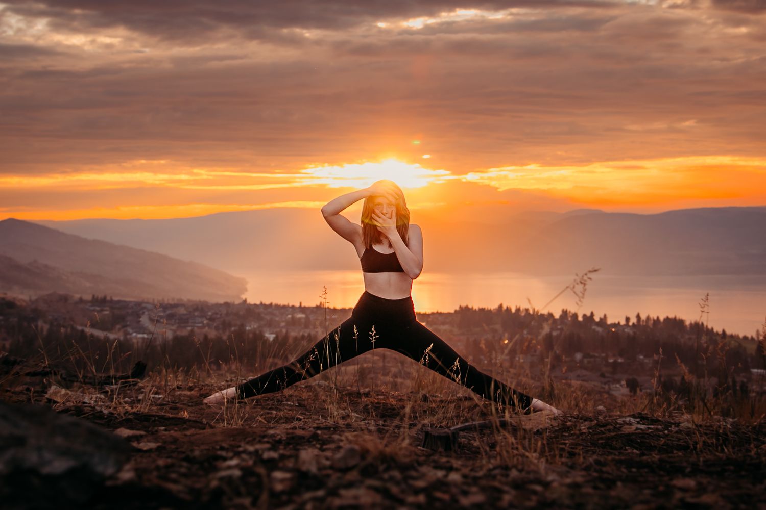 Silhouetted figure jumps with legs split against vibrant mountain sunset with dramatic orange sky.
