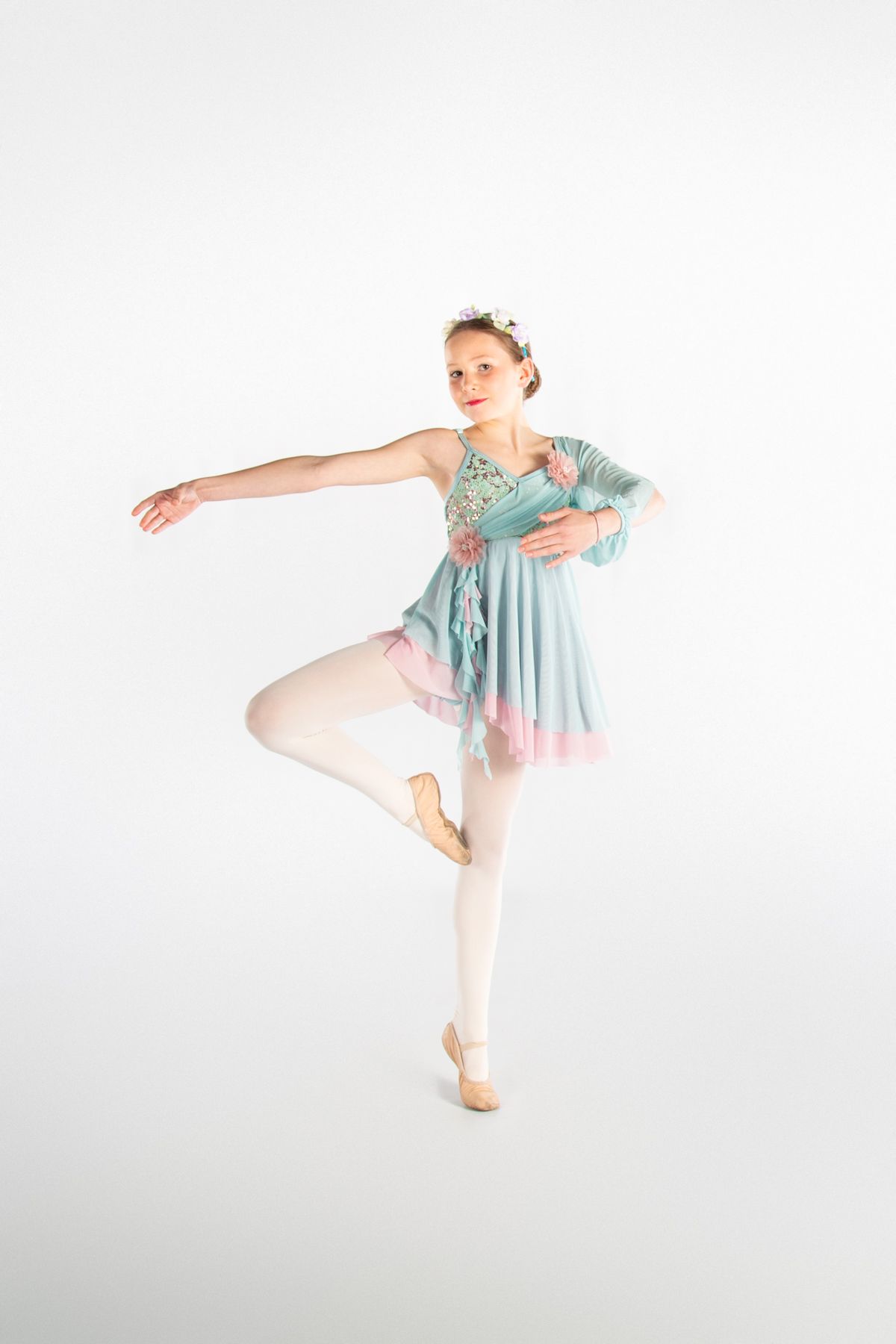 Ballet dancer in flowing mint dress performs graceful pose on white background.