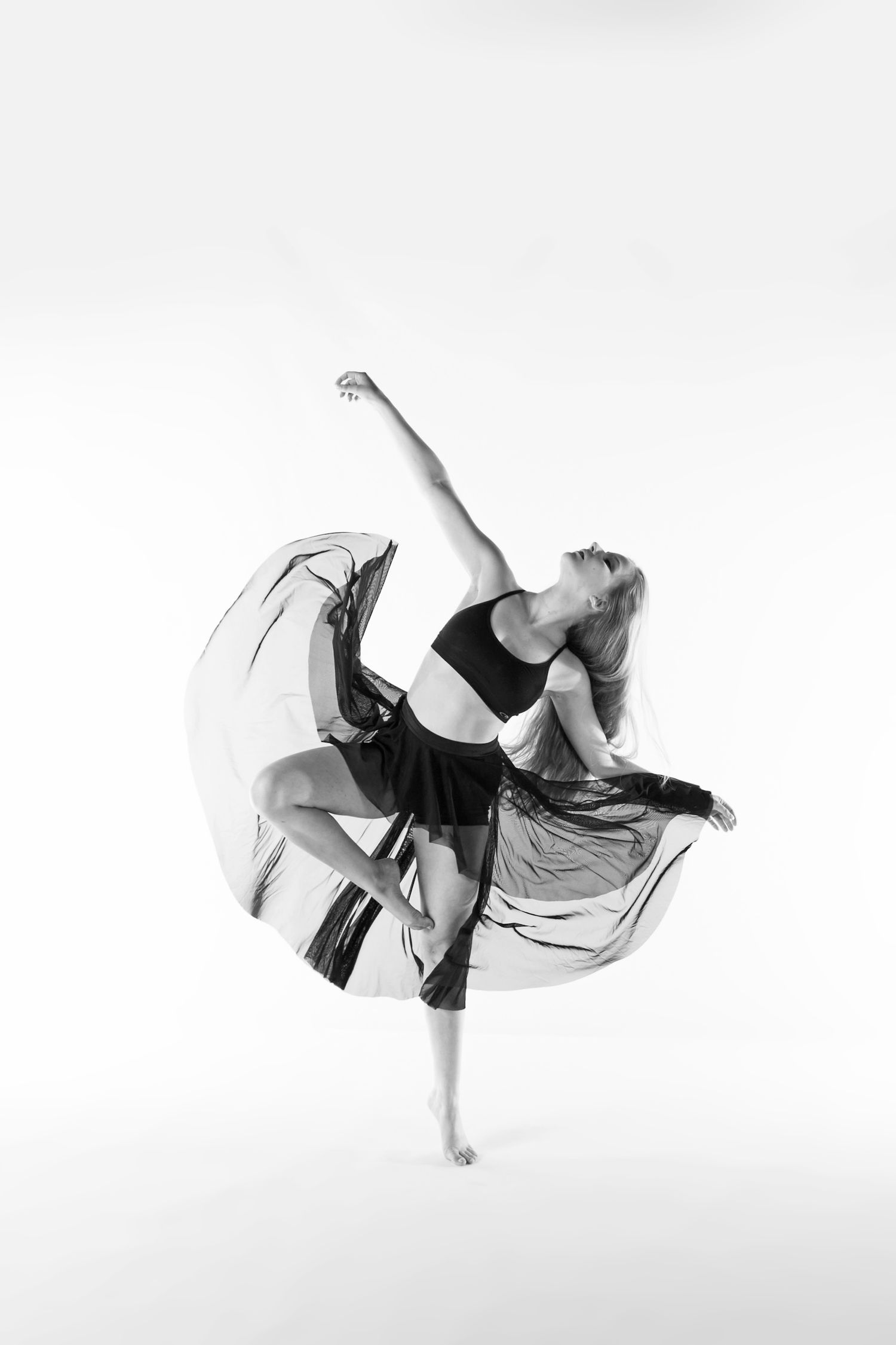 Dancer in flowing black dress executes dramatic pose during artistic performance.