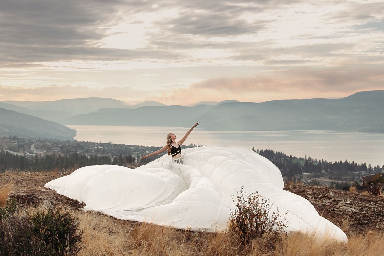 A dancer in a flowing white dress leaps gracefully against a backdrop of misty mountains and cloudy skies.