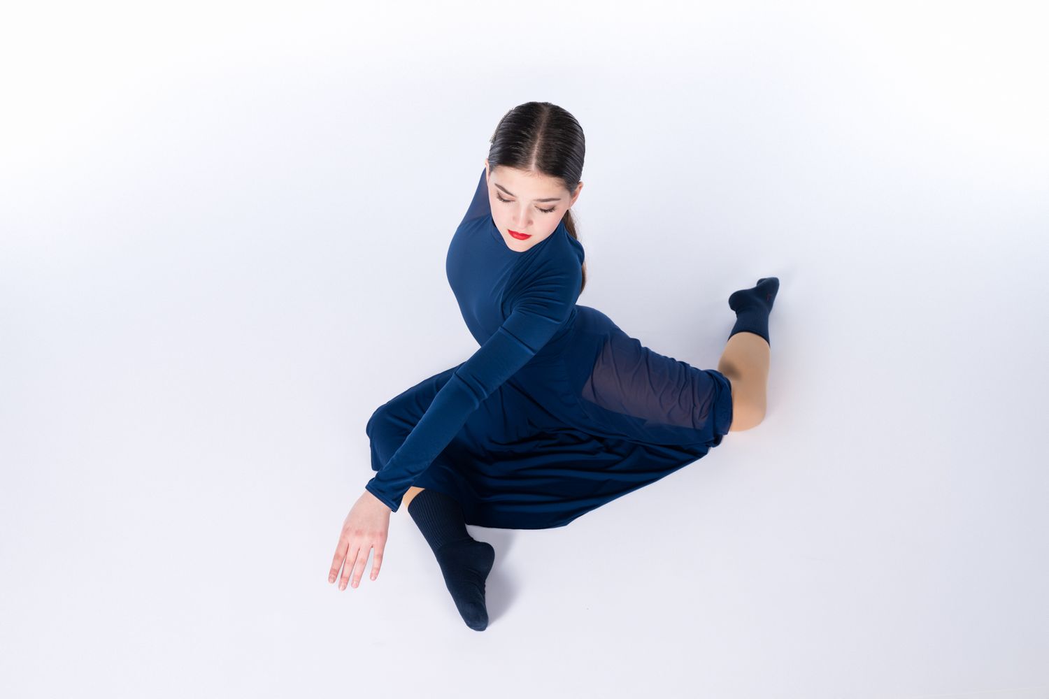 Dancer in navy blue outfit performs dynamic jump pose against white studio background.