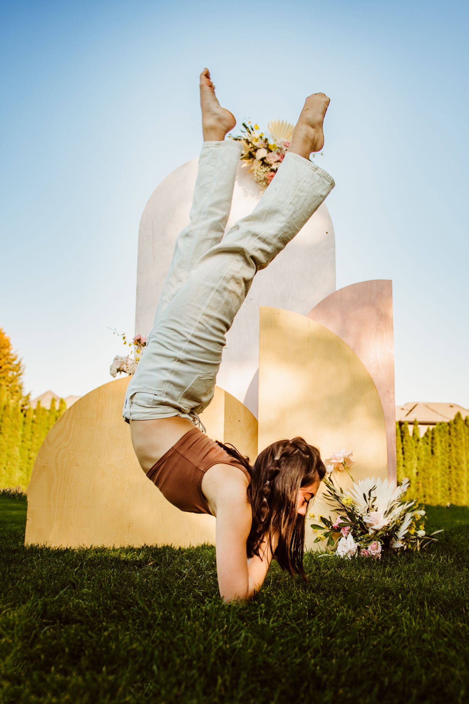 Dancer performs a graceful handstand pose against a blue sky backdrop with artistic white sculptural elements.