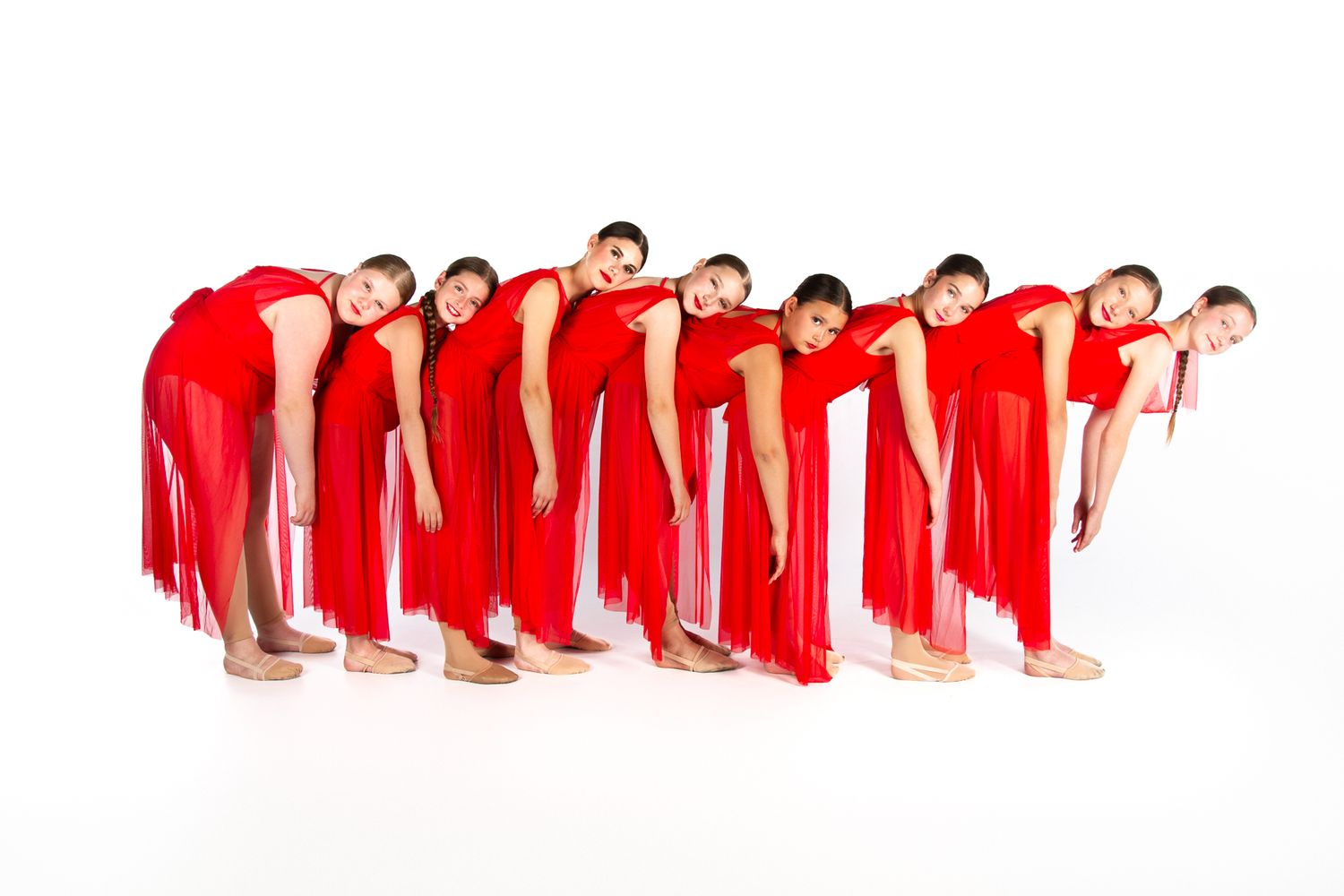 Dancers in bright red dresses creating a synchronized diagonal line formation against a white background.