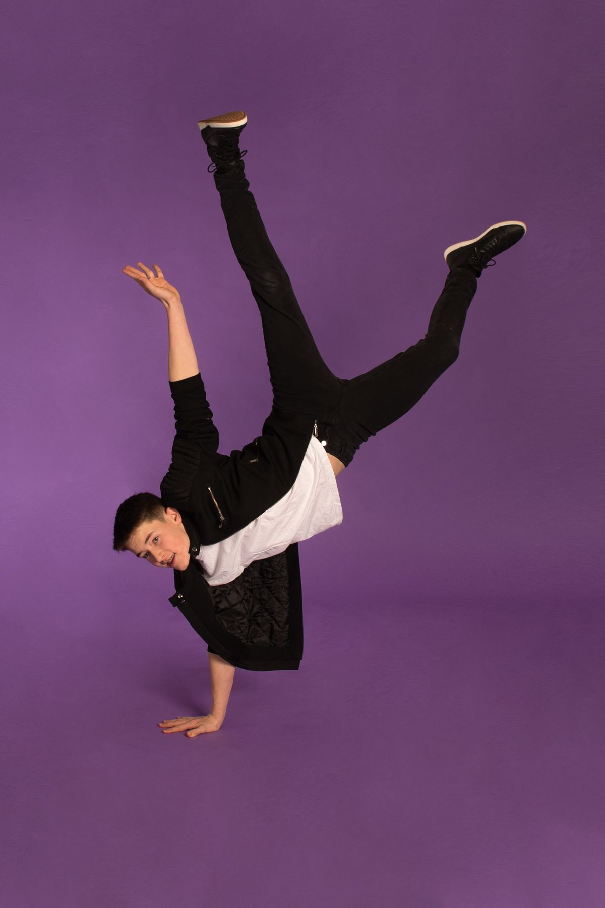 Dancer performs dynamic breakdance freeze on one hand against purple background while wearing black and white outfit.