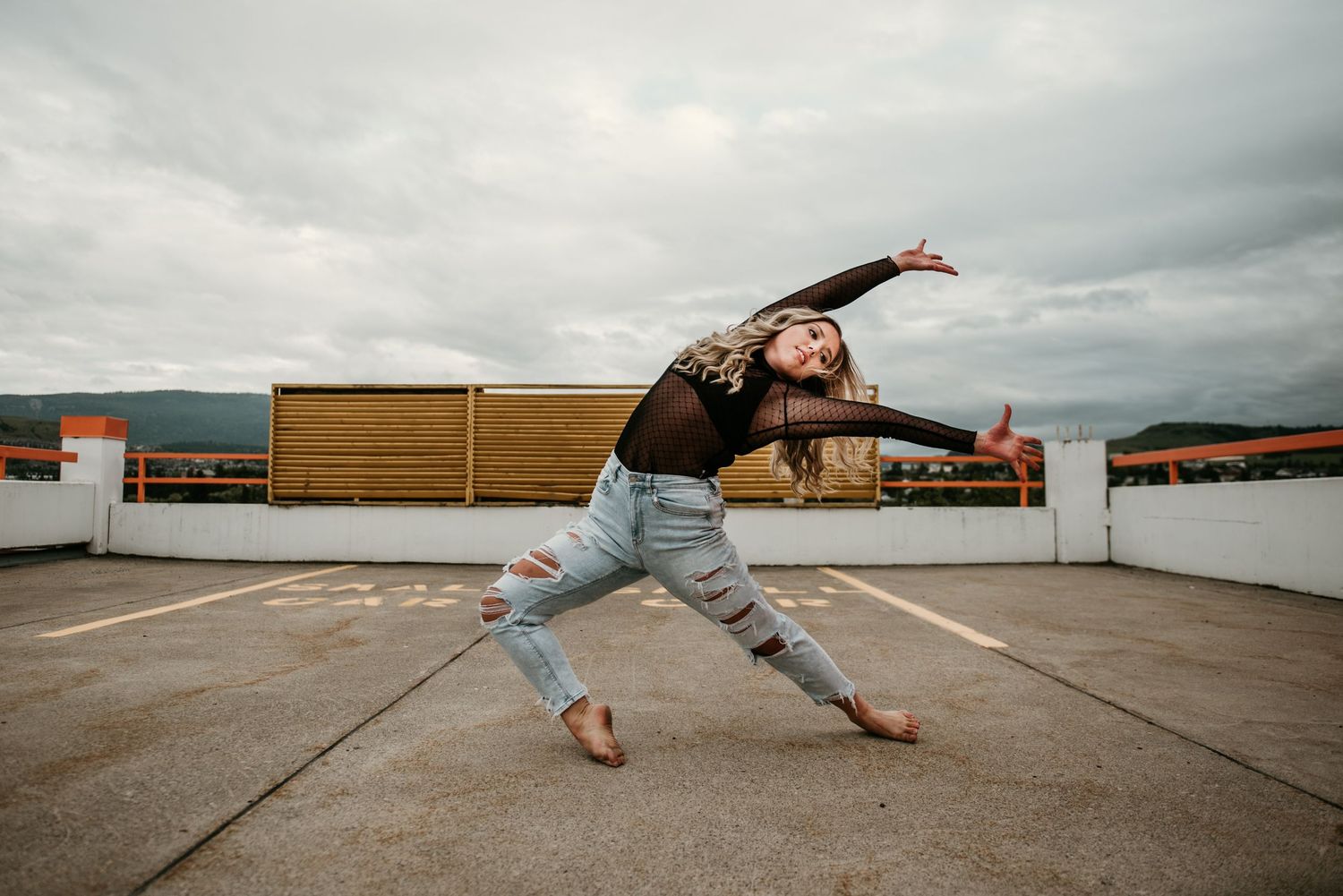 A dancer performs an expressive urban contemporary dance move on a rooftop under cloudy skies.
