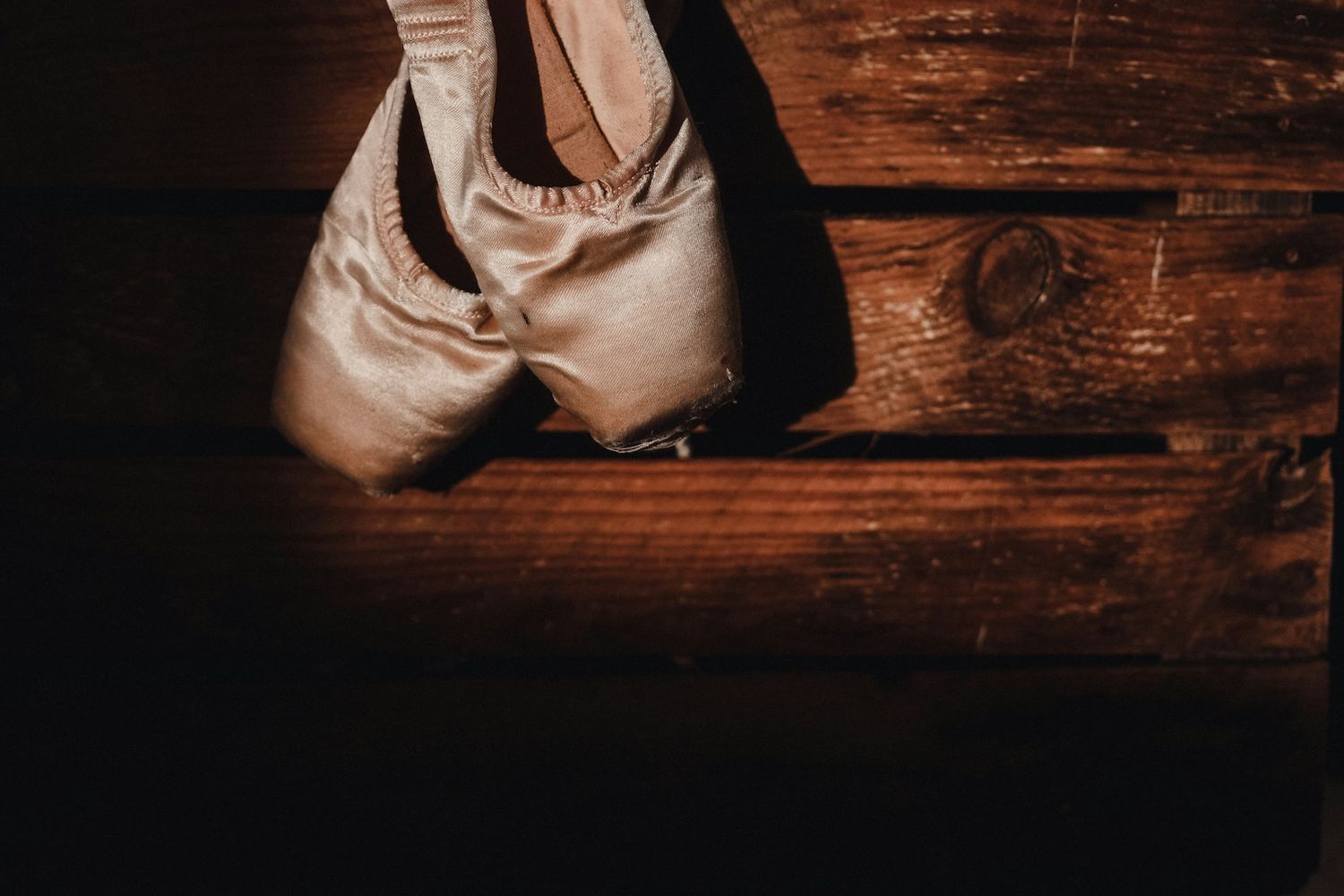 A pair of worn ballet pointe shoes resting on a dark wooden surface.